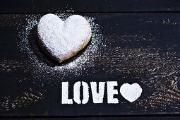A heart-shaped doughnut and the word 'Love' in icing sugar on a wooden surface