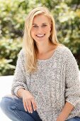 Junge blonde Frau in hellem Grobstrick-Pulli und Jeans