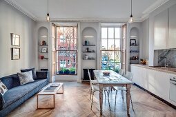 Fitted kitchen, dining table and sofa in open-plan interior of renovated townhouse apartment