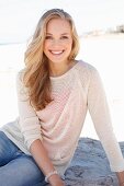 A young dark blonde woman on a beach wearing a light knitted jumper and jeans