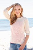 A young dark blonde woman on a beach wearing a light knitted jumper and jeans