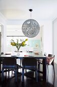 Ball lamp over black dining table in front of open kitchen