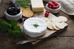 A cheese platter with sesame seed and wheat crackers, herbs, cherries and blackberries