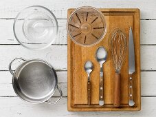Kitchen utensils: a saucepan, a glass bowl, a measuring cup, spoons, a whisk and a knife