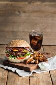 A beefburger with potato wedges, bacon, lettuce, cucumber, sour cream and a glass of cola