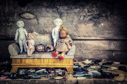 Knopfsammlung mit verschiedenen antiquarischen Miniatur-Puppen auf Puppenmöbel-Sofa vor düsterem Hintergrund