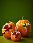 Drei Halloween-Kürbisse mit lustigen Gesichtern aus Obst und Gemüse