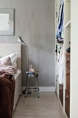 Metal stool used as bedside table against grey wall next to open-fronted cupboard