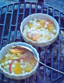 Small gratin dishes with slices of fruit and white chocolate on the barbecue