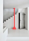 Red steel column in front of white concrete staircase next to rustic board door