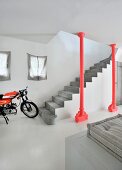 Concrete staircase behind red, industrial-style steel column and motorbike on pale concrete floor