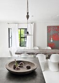 Bulbs of garlic in wooden bowl on concrete counter in front of rustic dining table and white Panton chairs