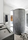 Concrete cylindrical shower in bathroom with concrete sink and vintage wooden stool