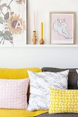 Pink and yellow patterned scatter cushions on sofa below pictures on narrow shelf