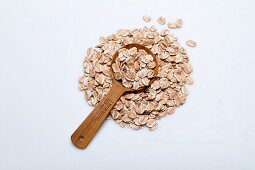 A pile of spelt flakes with a wooden spoon on a white surface
