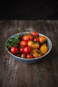 Various types of tomatoes in a bowl on a wooden surface