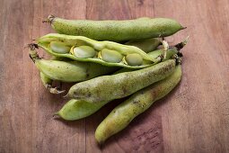 Broad beans in pods on a wooden surface