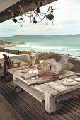 Flotsam and wooden figurines on weathered coffee table on castors on wooden deck with sea view