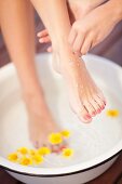 A woman taking a foot bath and having sea salt scrub rubbed into her feet