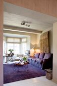 Purple couch and matching rug in comfortable lounge area in front of bright bay window