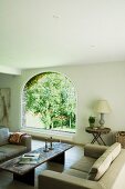 Rustic coffee table in comfortable lounge and view of garden through arched window