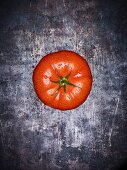 A beef tomato with droplets of water on a grey surface (seen from above)