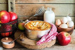 A sponge apple cake in a cake tin surrounded by ingredients