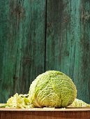 A whole and chopped savoy cabbage on a wooden board