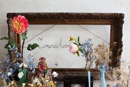 Vintage-style flower arrangement in front of antique picture frame around hand-written motto on wall