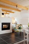 Comfortable armchair next to fireplace in country house with wood-beamed ceiling and black floor tiles