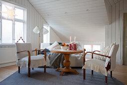 Table with pedestal base and old chair with loose cover under sloping ceiling