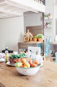 Stainless steel kitchen furnishings and fruit bowl on rustic dining table below white gallery in loft apartment