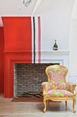 Antique armchair with neon upholstery in front of traditional fireplace painted with red, white and black stripes
