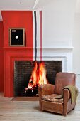 Vintage leather armchair in front of fire in traditional fireplace painted with red, white and black stripes