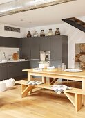 Wooden table and benched on oak parquet floor in front of grey kitchen