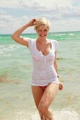 Blonde Frau in buntem Bikini mit weißem T-Shirt darüber am Strand