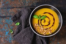 Black ceramic bowl of pumpkin and sweet potato cream soup with fresh basil, fried onion and balsamic sauce