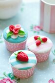 Cupcakes mit Erdbeeren und Rosen aus Fondant in rosa gepunkteten Förmchen