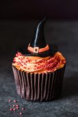 A halloween cupcake with orange buttercream an a witches' hat