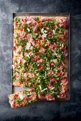 Pizza with Parma ham and herbs on a baking tray