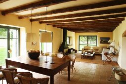 Fireplace, tiled floor and wood-beamed ceiling in open-plan living area of renovated country house