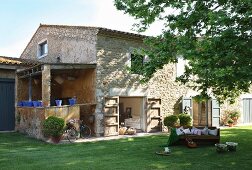 Guitar on wooden bench on lawn outside open terrace doors of renovated stone house