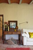 Table with drawers next to standard lamp and white couch in country-house interior