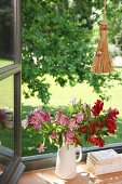 Flowers in white jug next to stacked books on sill of open window