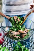 A man is mixing grilled steak with fresh herbs