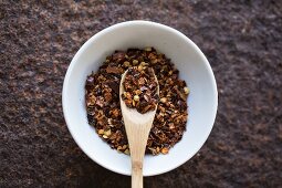 Chilli flakes with a wooden spoon in a bowl (seen from above)