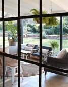 Blick durch Industrieverglasung auf überdachte, möblierte Terrasse und sommerlichen Garten