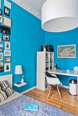 weiße Schreibtischplatte mit offenem Regal in Schlafzimmer mit hellblauen Wänden und Bildergalerie