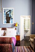 Bed with leopard-print elements against pale blue wall and view into bathroom