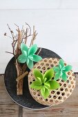 Grüne Origami-Blüten auf einem Ast und Bastkörbchen